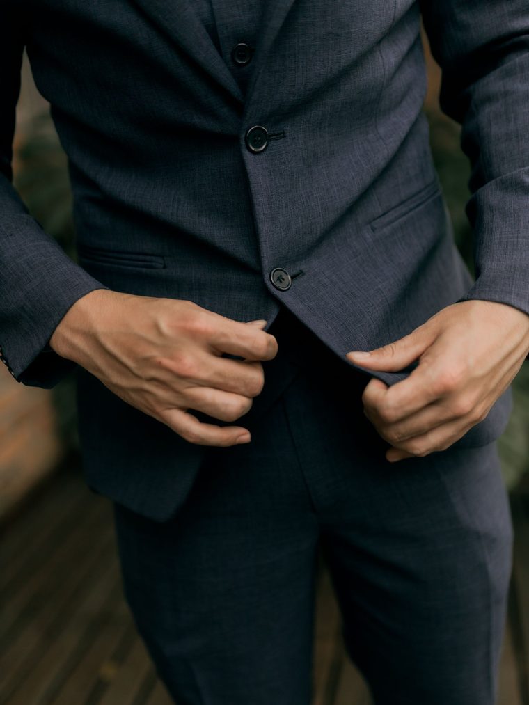 A man fastening the button of a navy tailored suit jacket.